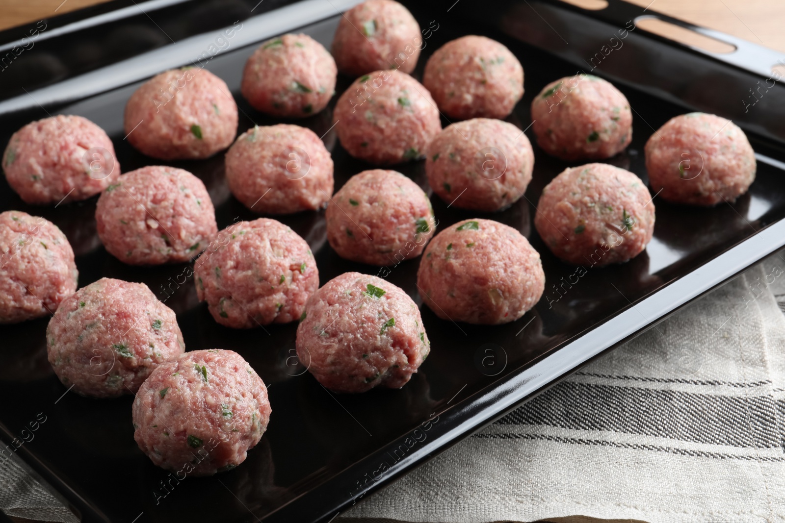 Photo of Baking dish with many fresh raw meatballs on kitchen towel