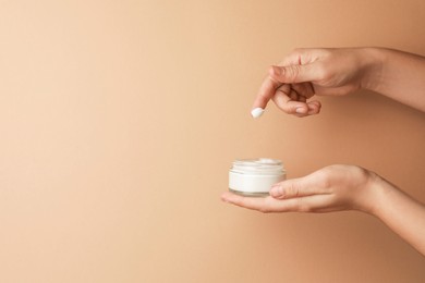 Woman applying face cream on beige background, closeup. Space for text