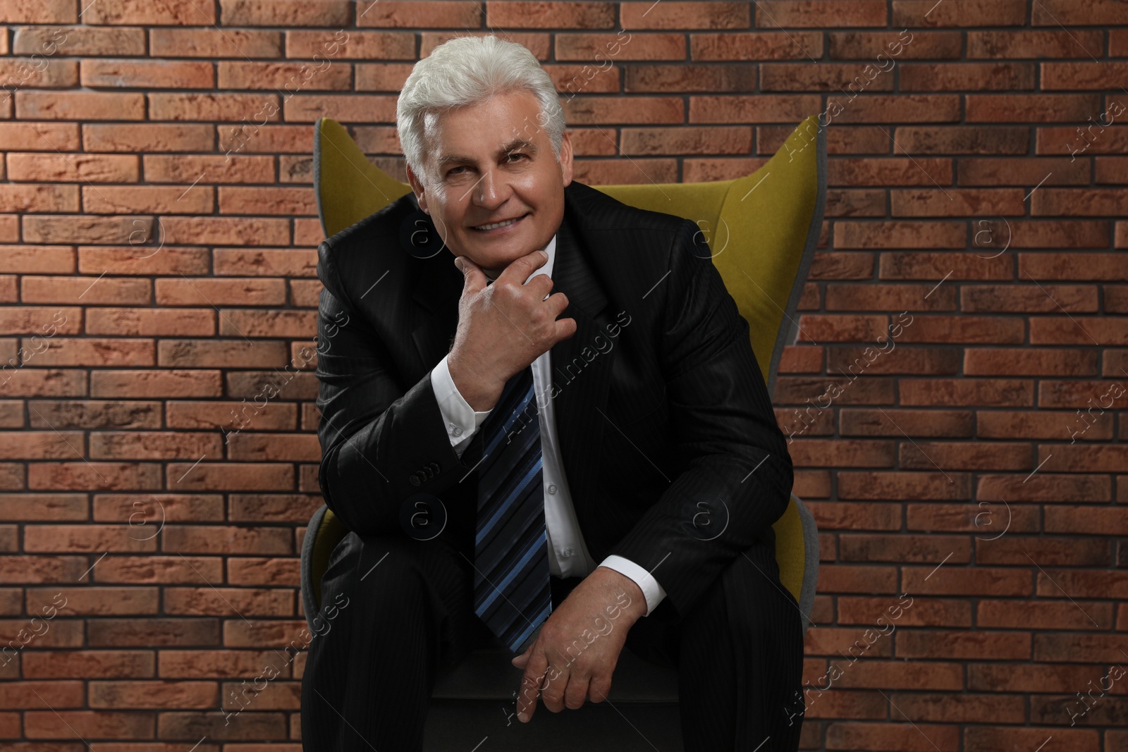 Photo of Happy mature businessman sitting in armchair near brick wall