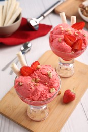 Photo of Delicious scoops of strawberry ice cream with wafer sticks and nuts in glass dessert bowls served on white wooden table, above view