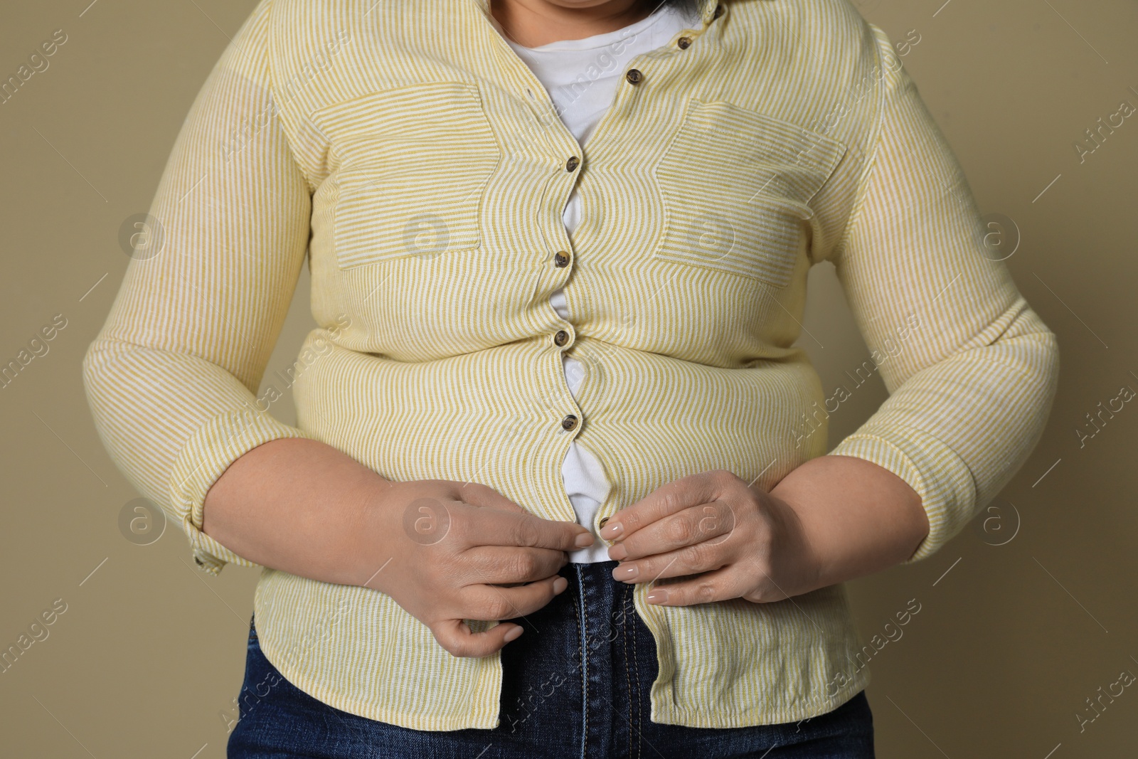 Photo of Overweight woman trying to button up tight shirt on beige background, closeup