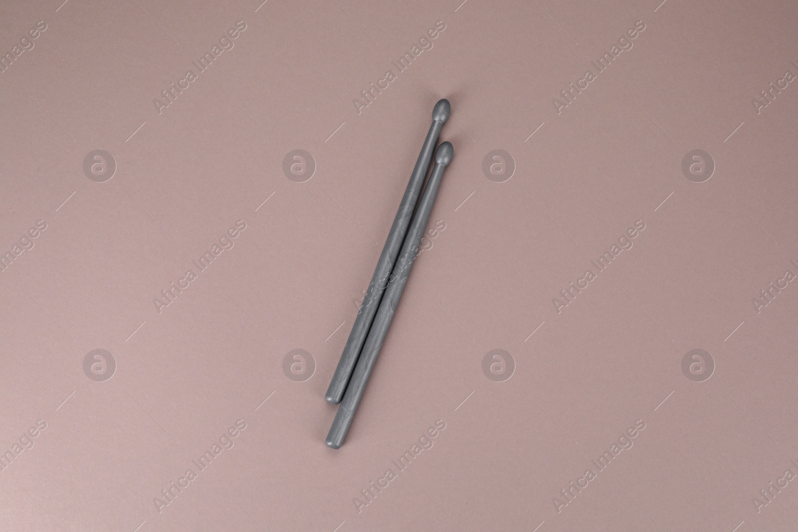 Photo of Two gray drum sticks on dusty rose background, top view