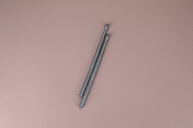 Photo of Two gray drum sticks on dusty rose background, top view