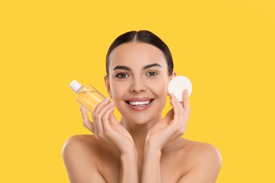 Photo of Beautiful woman holding makeup remover and cotton pad on yellow background