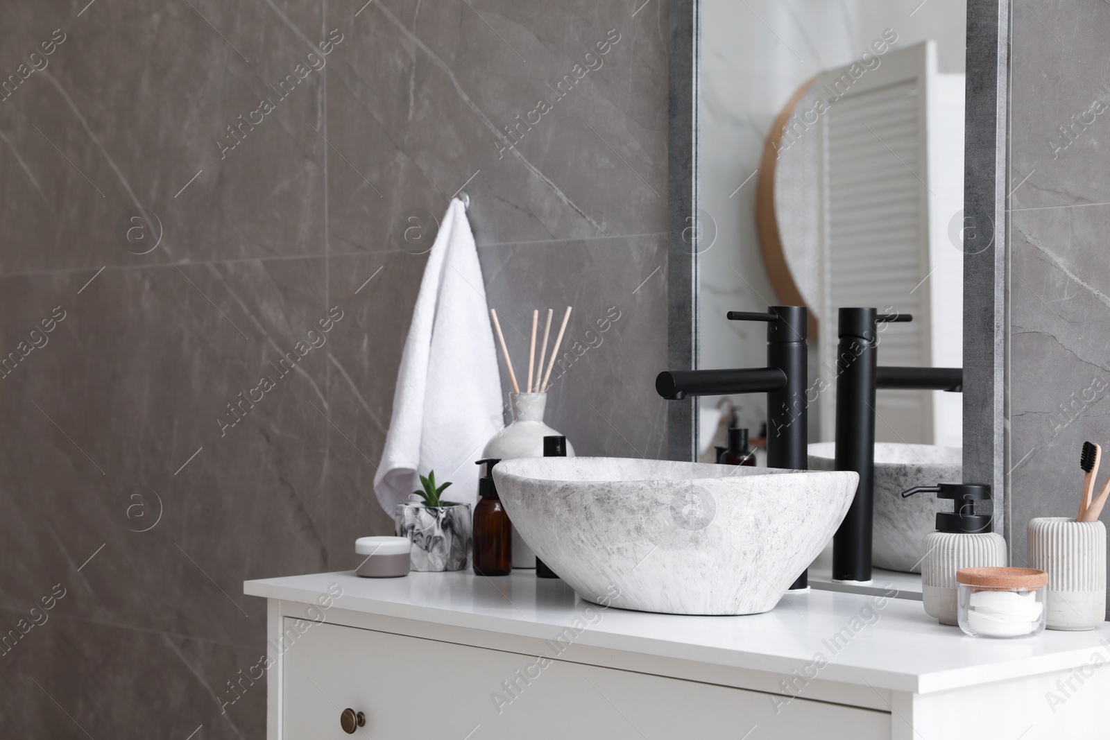 Photo of Stone vessel sink with faucet and toiletries on white countertop in bathroom