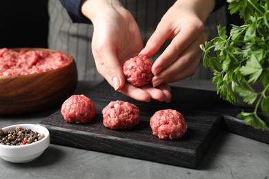 Photo of Woman making meatball from ground meat at grey table, closeup