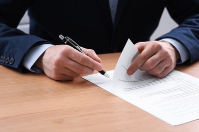 Businessman signing contract at wooden table, closeup of hands