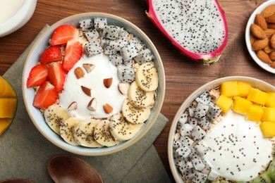 Bowls of granola with yogurt and fruits on wooden table, flat lay