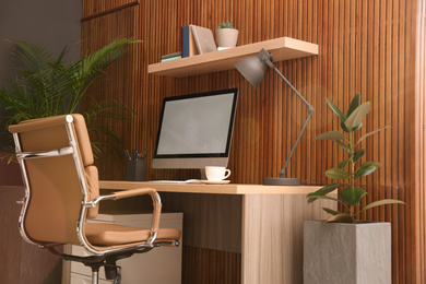 Photo of Comfortable workplace with computer near wooden wall in stylish room interior. Home office design