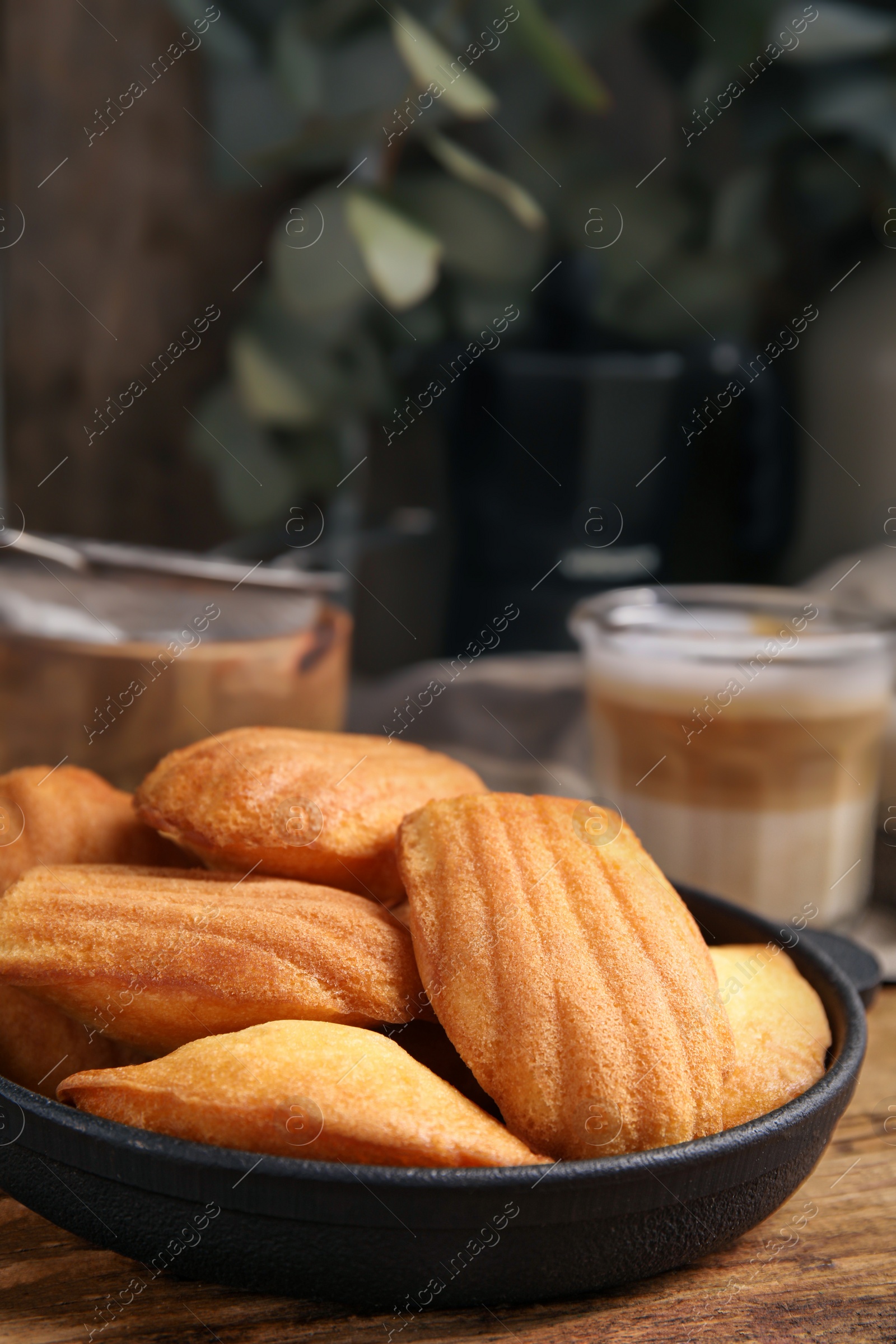 Photo of Delicious madeleine cakes in frying pan on wooden table, closeup. Space for text