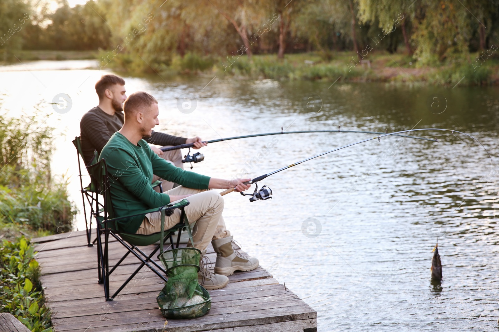 Photo of Friends fishing on wooden pier at riverside. Recreational activity