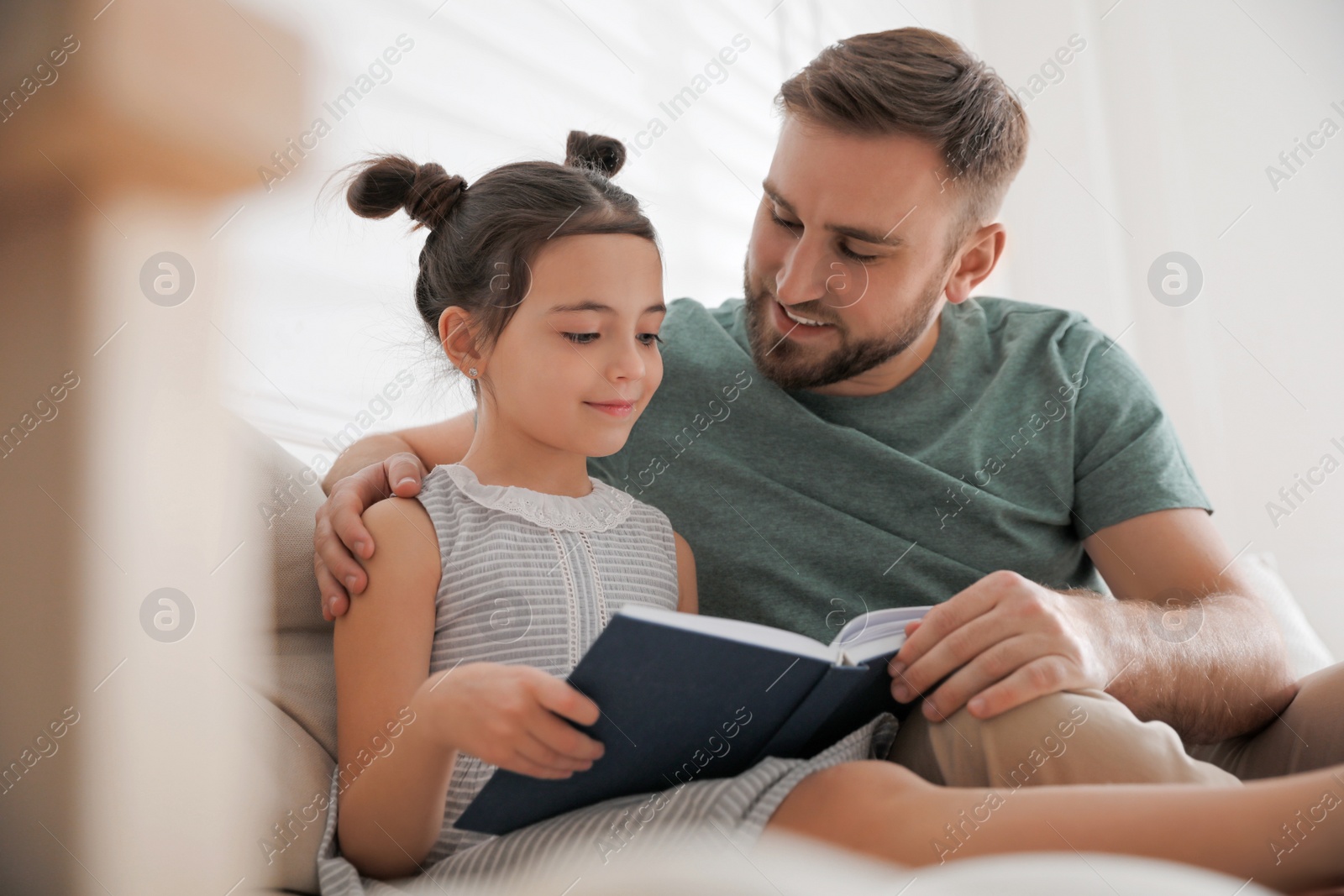 Photo of Little girl with father reading fairy tale in living room