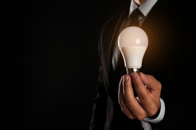 Photo of Businessman holding lamp bulb against dark background, closeup. Space for text
