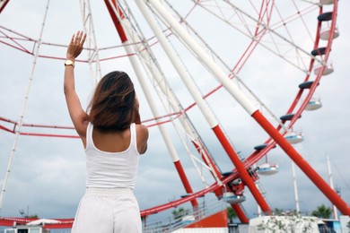 Photo of Young woman near Ferris wheel outdoors, back view. Space for text