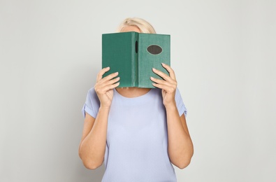 Mature woman reading book on light background