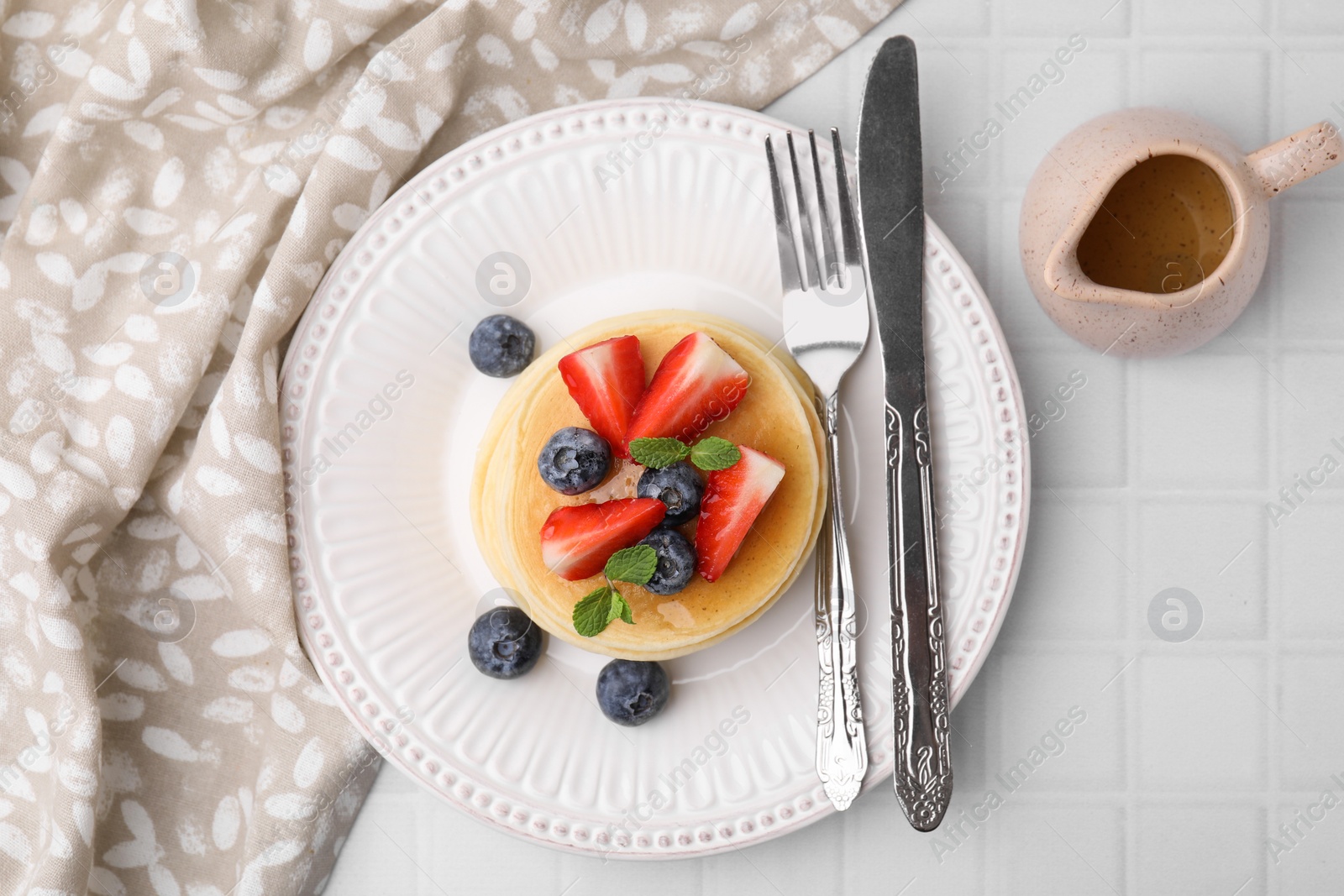 Photo of Delicious pancakes with strawberries, blueberries and mint served on white tiled table, top view