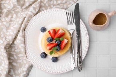 Delicious pancakes with strawberries, blueberries and mint served on white tiled table, top view