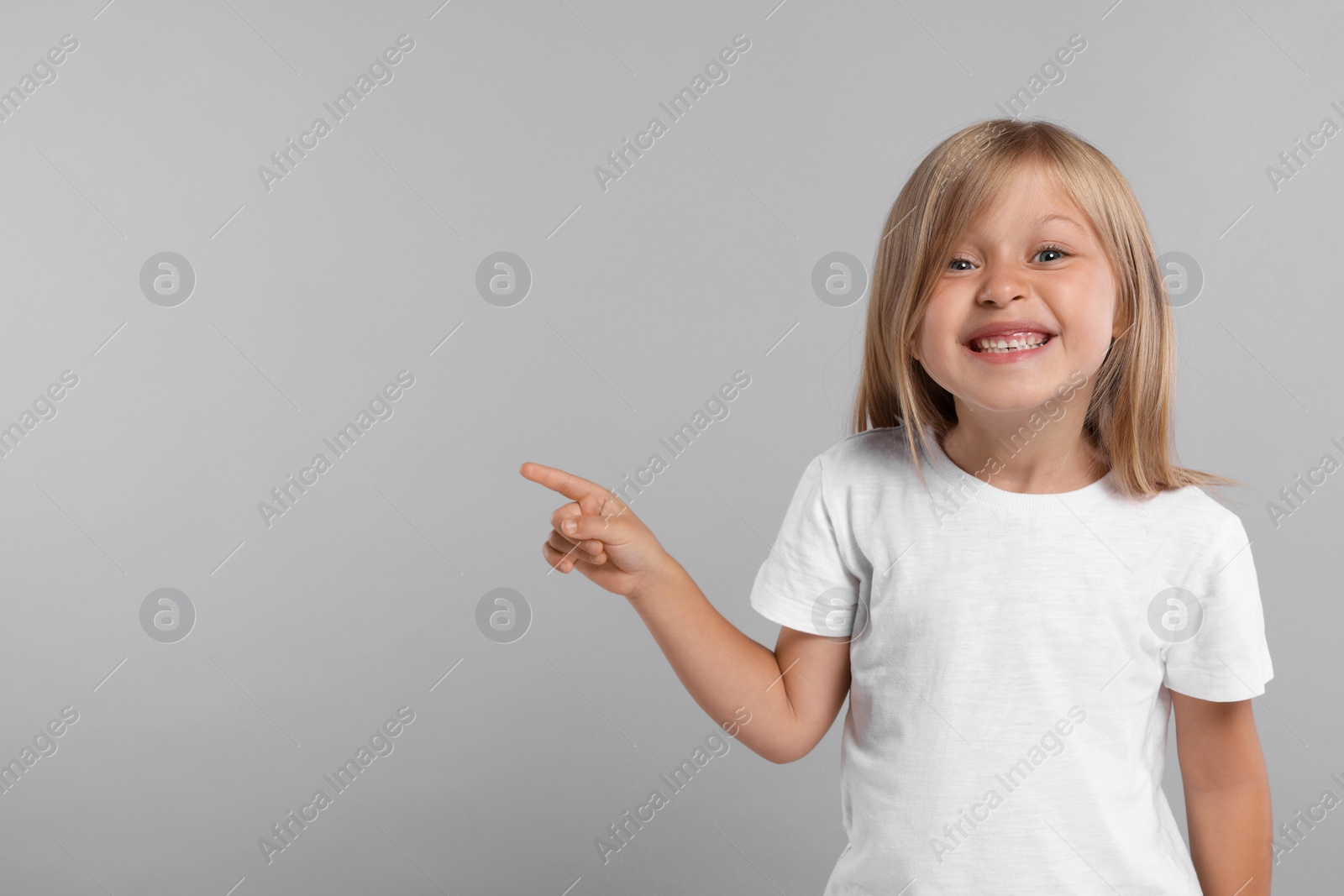 Photo of Special promotion. Smiling girl pointing at something on grey background. Space for text