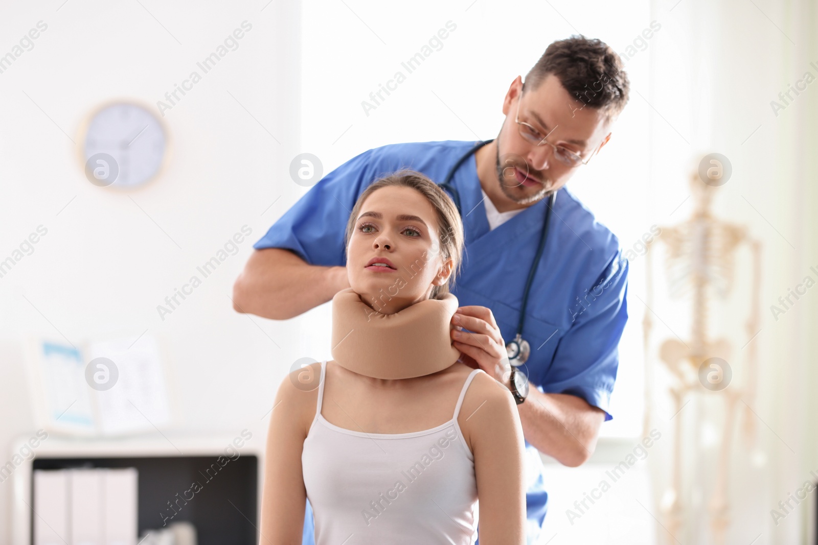 Photo of Male orthopedist applying cervical collar onto patient's neck in clinic