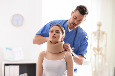 Male orthopedist applying cervical collar onto patient's neck in clinic