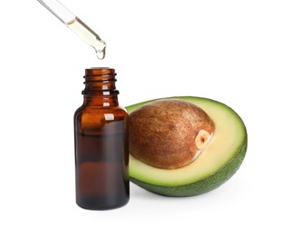 Photo of Dripping essential oil into bottle near cut avocado on white background
