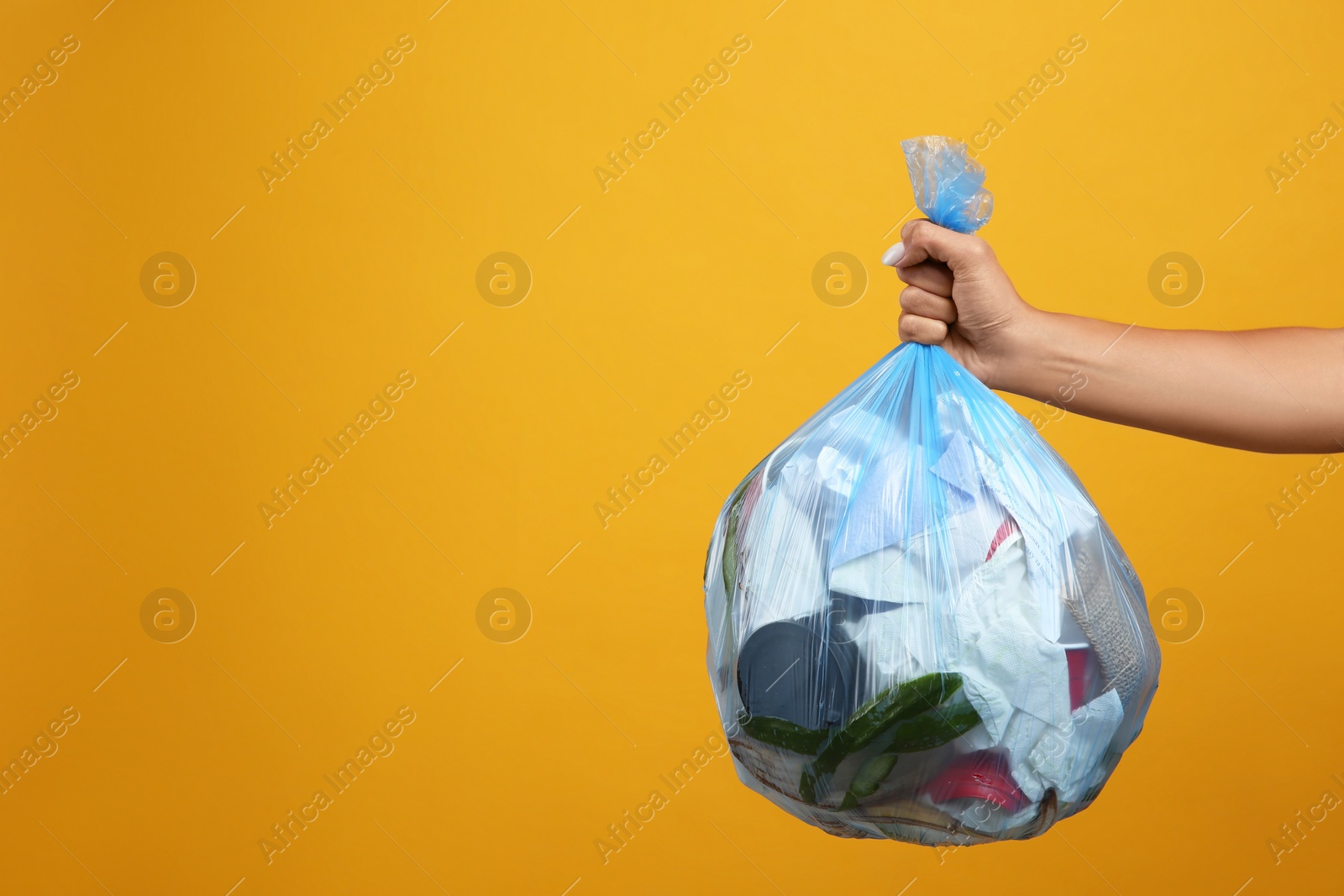 Photo of Woman holding full garbage bag on yellow background, closeup. Space for text