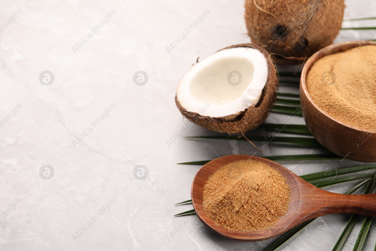 Photo of Spoon with coconut sugar, palm leaves, bowl and fruit on light marble table, closeup. Space for text