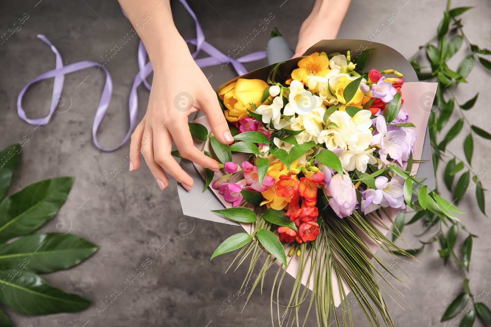 Photo of Woman making beautiful bouquet of freesia flowers on grey background