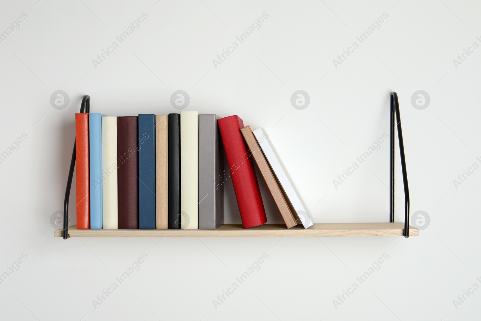 Photo of Wooden shelf with many hardcover books on white wall