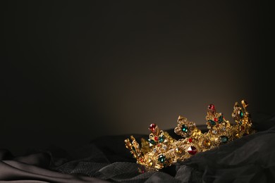 Photo of Beautiful golden crown with gems on dark cloth. Space for text