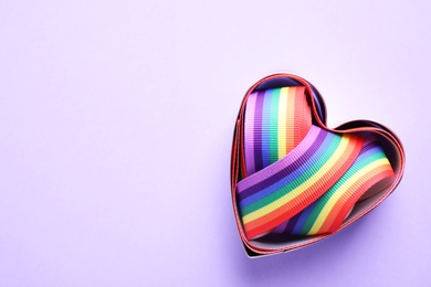 Photo of Heart shaped mold and bright rainbow ribbon on color background, top view with space for text. Symbol of gay community