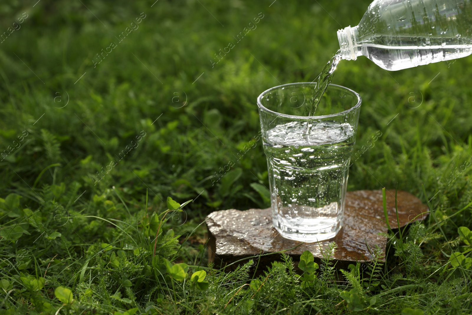 Photo of Pouring fresh water from bottle into glass on stone outdoors. Space for text