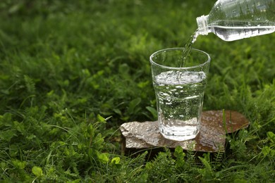 Pouring fresh water from bottle into glass on stone outdoors. Space for text