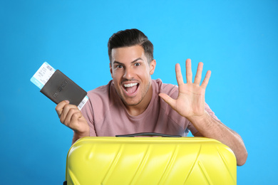 Photo of Excited man with suitcase and ticket in passport for summer trip on blue background. Vacation travel