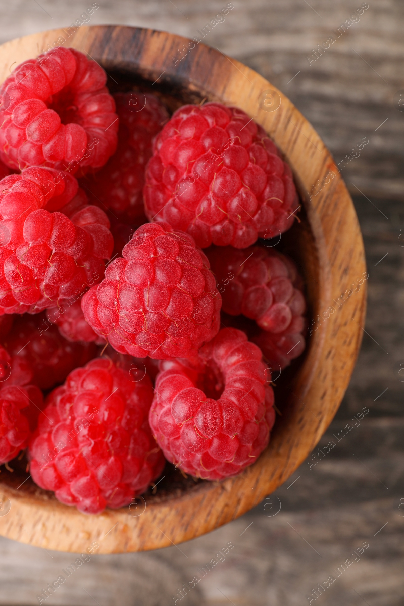 Photo of Tasty ripe raspberries in bowl on wooden table, top view