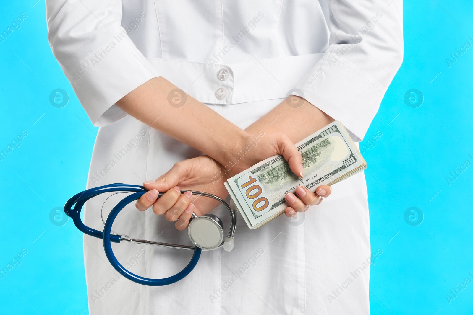 Photo of Doctor with bribe and stethoscope on light blue background, closeup. Corruption in medicine