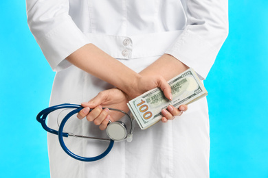 Doctor with bribe and stethoscope on light blue background, closeup. Corruption in medicine