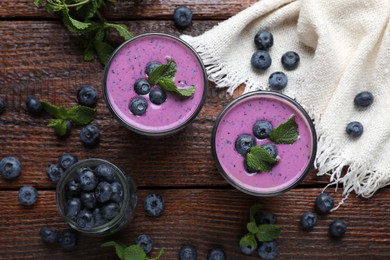 Glasses of blueberry smoothie with mint and fresh berries on wooden table, flat lay