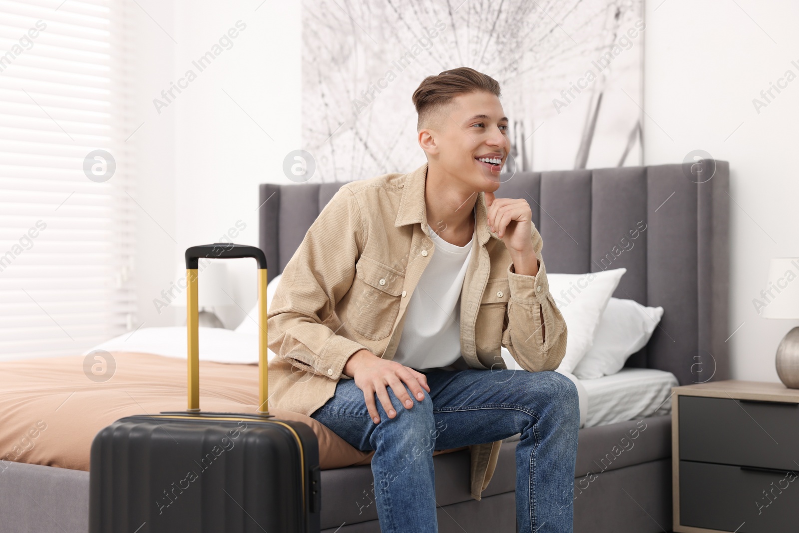 Photo of Smiling guest with suitcase on bed in stylish hotel room