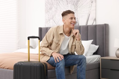 Smiling guest with suitcase on bed in stylish hotel room