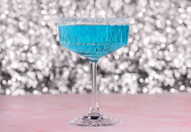Photo of Glass of refreshing light blue drink on pink marble table against blurred background