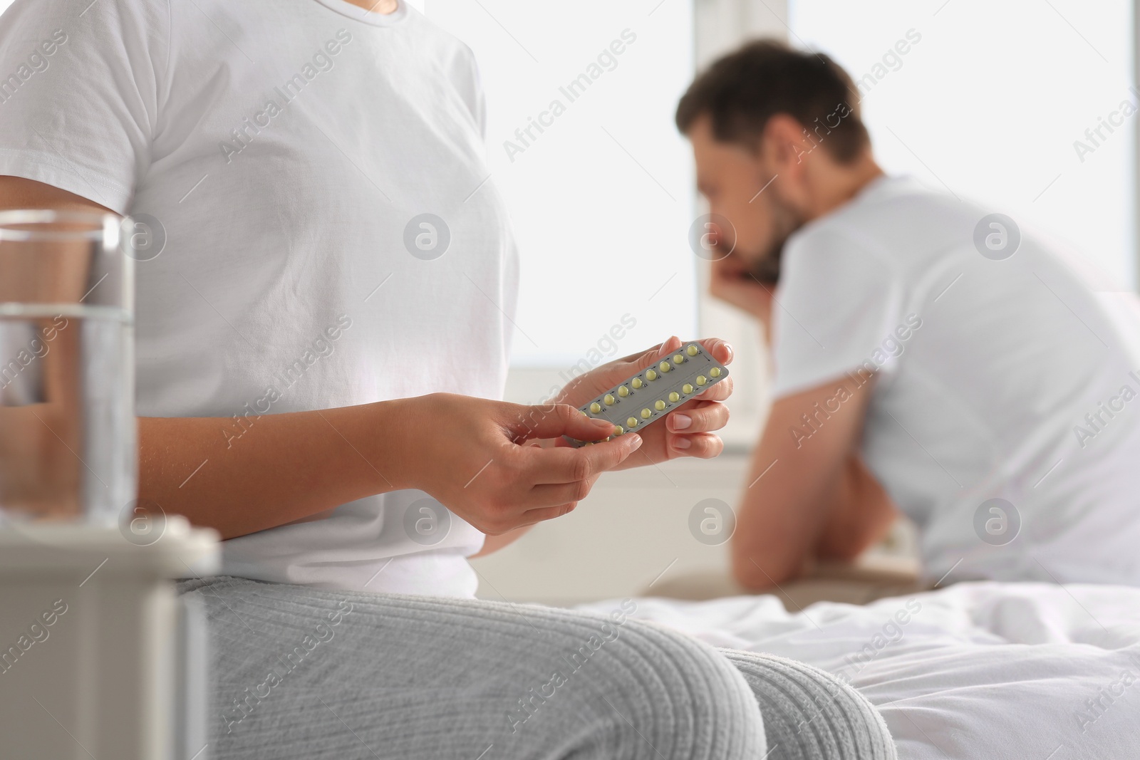 Photo of Couple in bedroom. Woman with blister of oral contraception pills, closeup