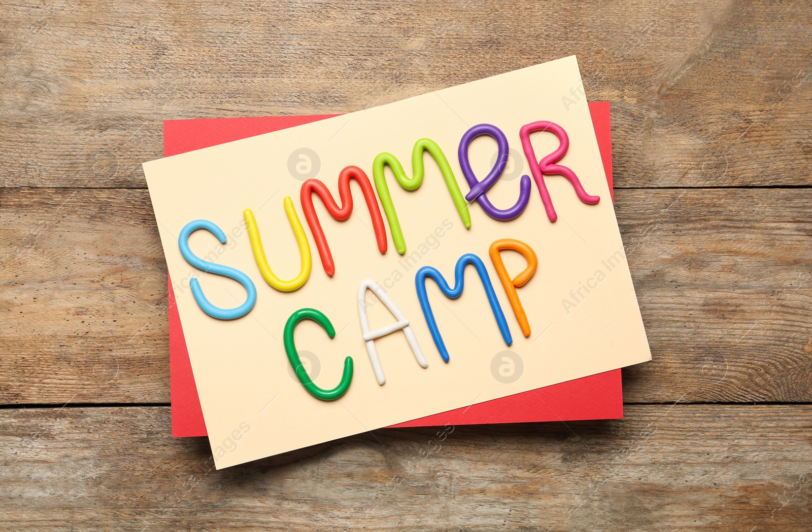 Photo of Text SUMMER CAMP made of modelling clay on wooden table, flat lay