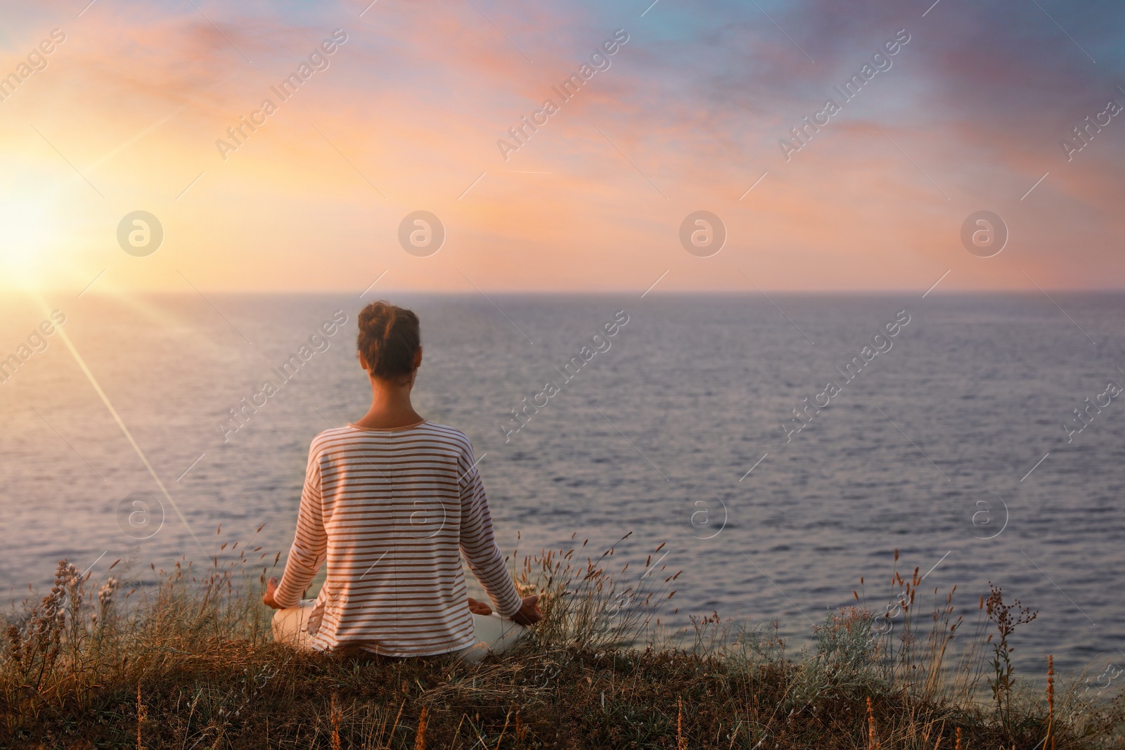 Image of Woman meditating near sea at sunrise, back view. Practicing yoga