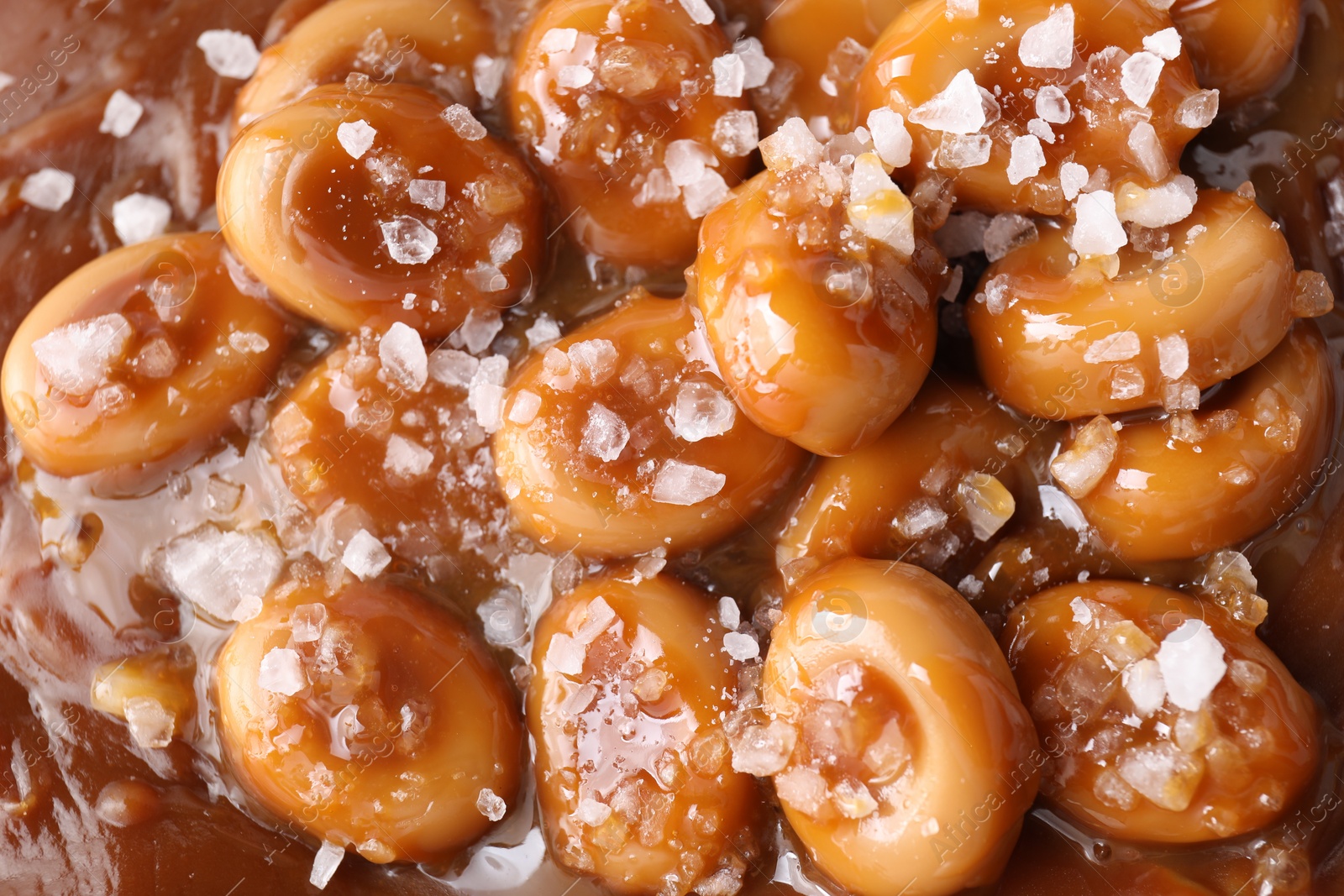 Photo of Tasty candies, caramel sauce and salt as background, top view