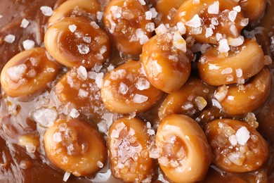 Tasty candies, caramel sauce and salt as background, top view