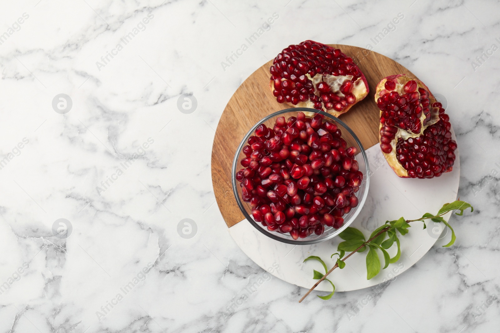 Photo of Ripe juicy pomegranate grains and green leaves on white marble table, top view. Space for text