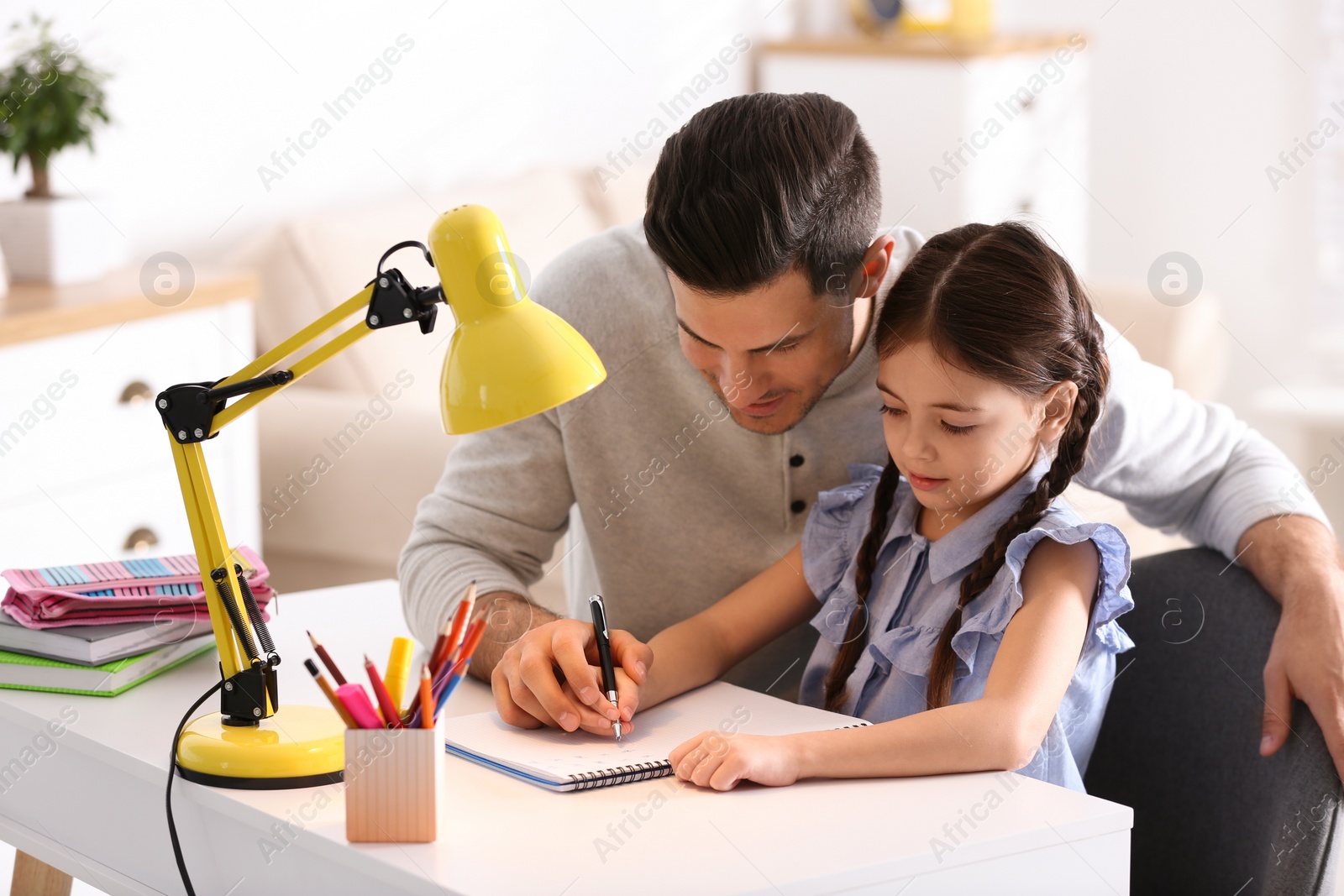 Photo of Man helping his daughter with homework at table indoors