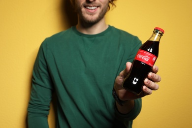 MYKOLAIV, UKRAINE - NOVEMBER 28, 2018: Young man with bottle of Coca-Cola on color background, closeup