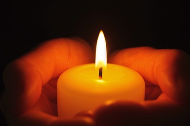 Photo of Young person holding burning candle in darkness, closeup